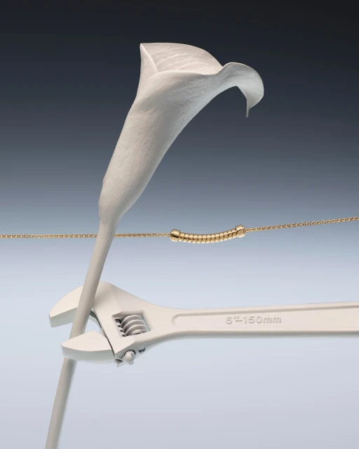 Still life of a white calla lily being held by a white wrench, with a gold necklace and dark gray to light gray background gradient.