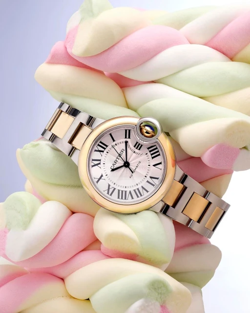 Luxury gold and silver Cartier watch on a two-tone bracelet, presented on a soft spiral of pastel marshmallows against a light background.