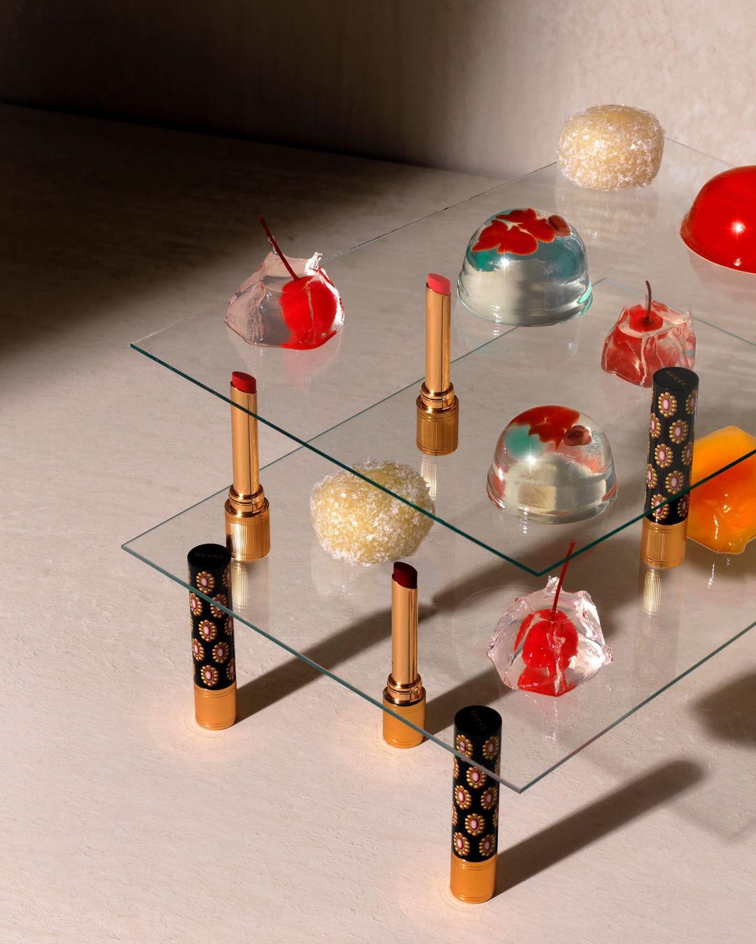 Still life with lipstick tubes and decorative candies on a tiered glass surface, showcasing beauty and food product photography.