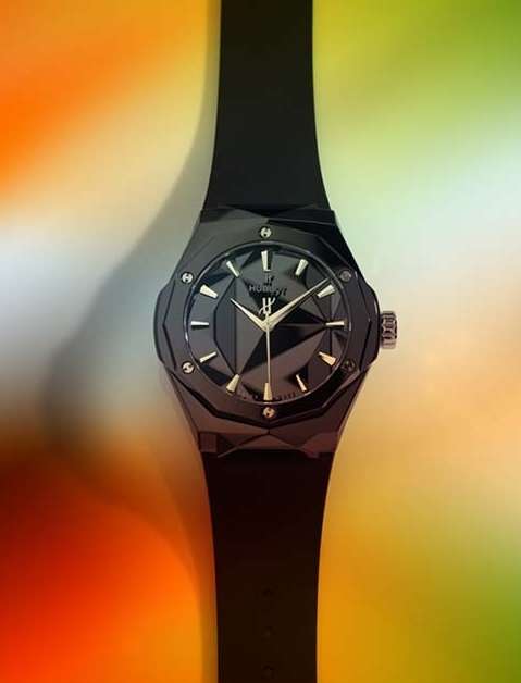 Close-up of a black Hublot watch featuring a geometric-faceted face and matching band, showcased against a vibrant background.