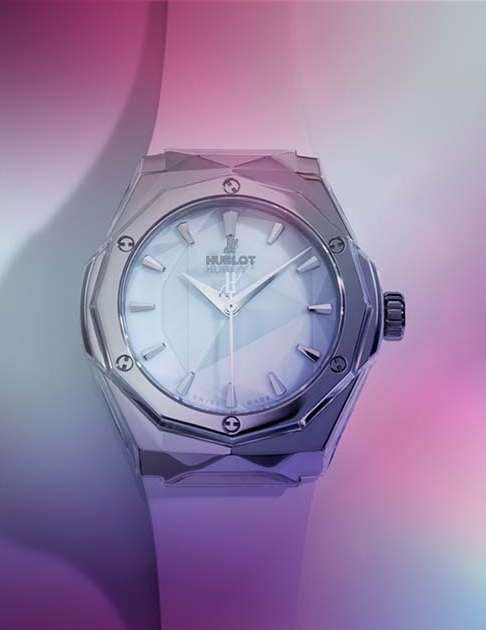 Close-up of a Hublot watch featuring a silver multifaceted design and mother-of-pearl dial against a soft, multi-colored backdrop.