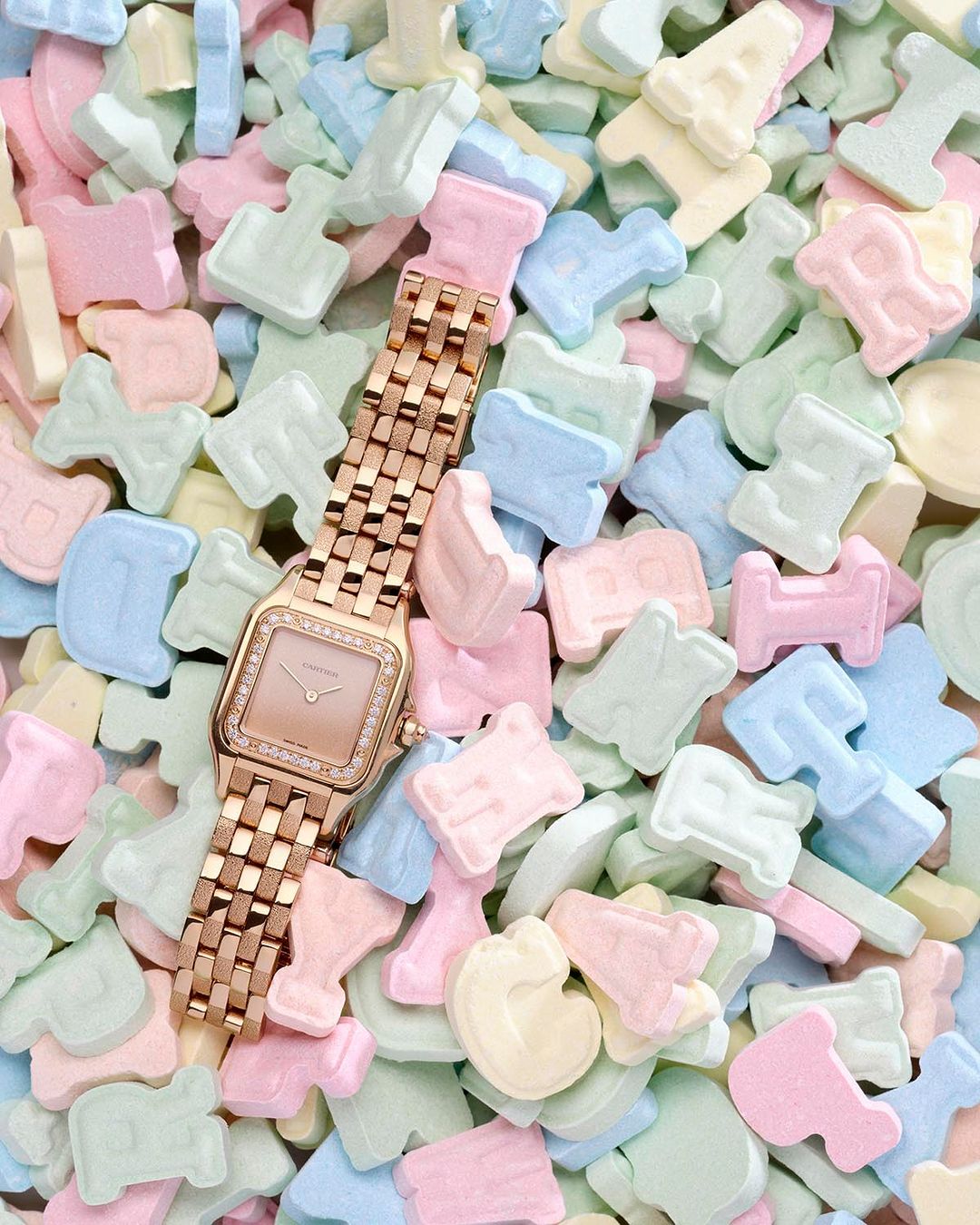 Rose gold wristwatch with a diamond bezel on a pile of pastel-colored candy letters, wristwear, jewelry, and fashion photography.
