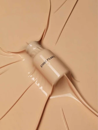 Makeup bottle surrounded by cosmetic foundation. Beige background, beauty product shot. ETOILE FILANTE text on the bottle.