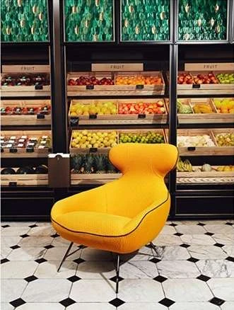Stylish yellow chair in a modern market with fresh fruit displayed on shelves, creating a vibrant and inviting shopping atmosphere.