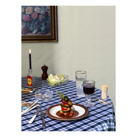 Still life shot of a plated zucchini tower with wine, salad, candle, cigarettes, and matches on a blue and white checkered tablecloth.