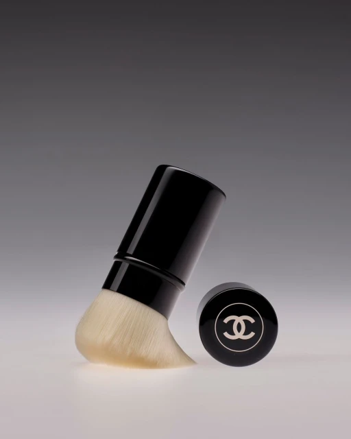 Chanel powder brush product shot on gray backdrop. Cosmetics still life shows a brush and logo of the Chanel brand.