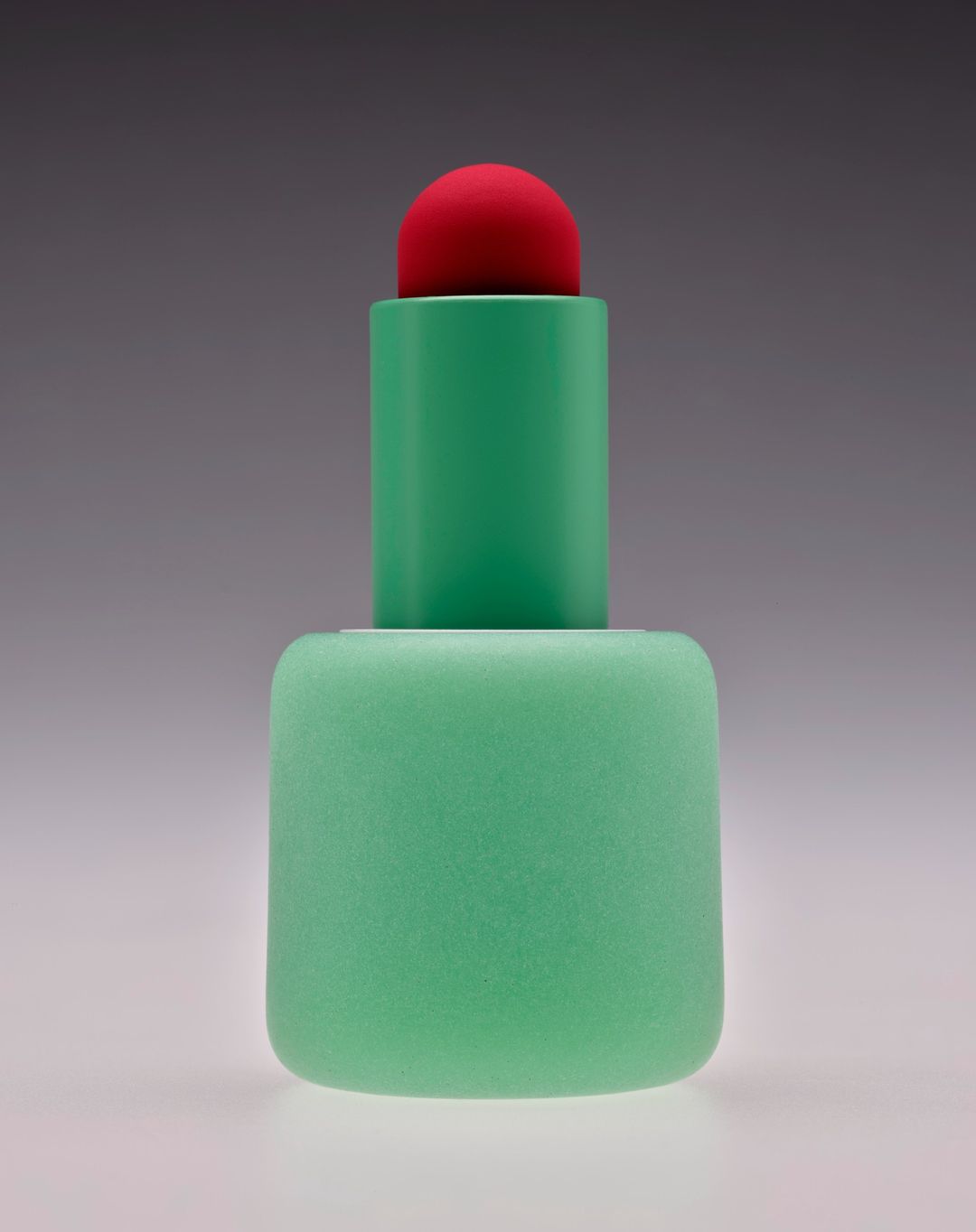 Minimalist studio shot of a geometric plastic sculpture in hues of green and red, set against a gradient gray background.