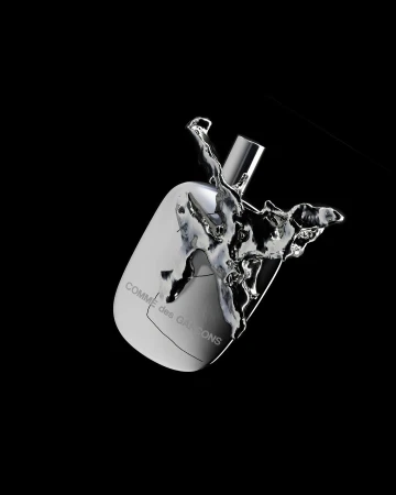 Studio shot of a reflective silver perfume bottle with liquid splashing around it on a black background, displaying the COMME des GARÇONS logo.