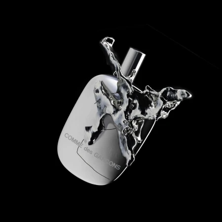 Comme des Garçons perfume bottle angled, surrounded by splash of silver liquid against a stark black background in a studio setting.