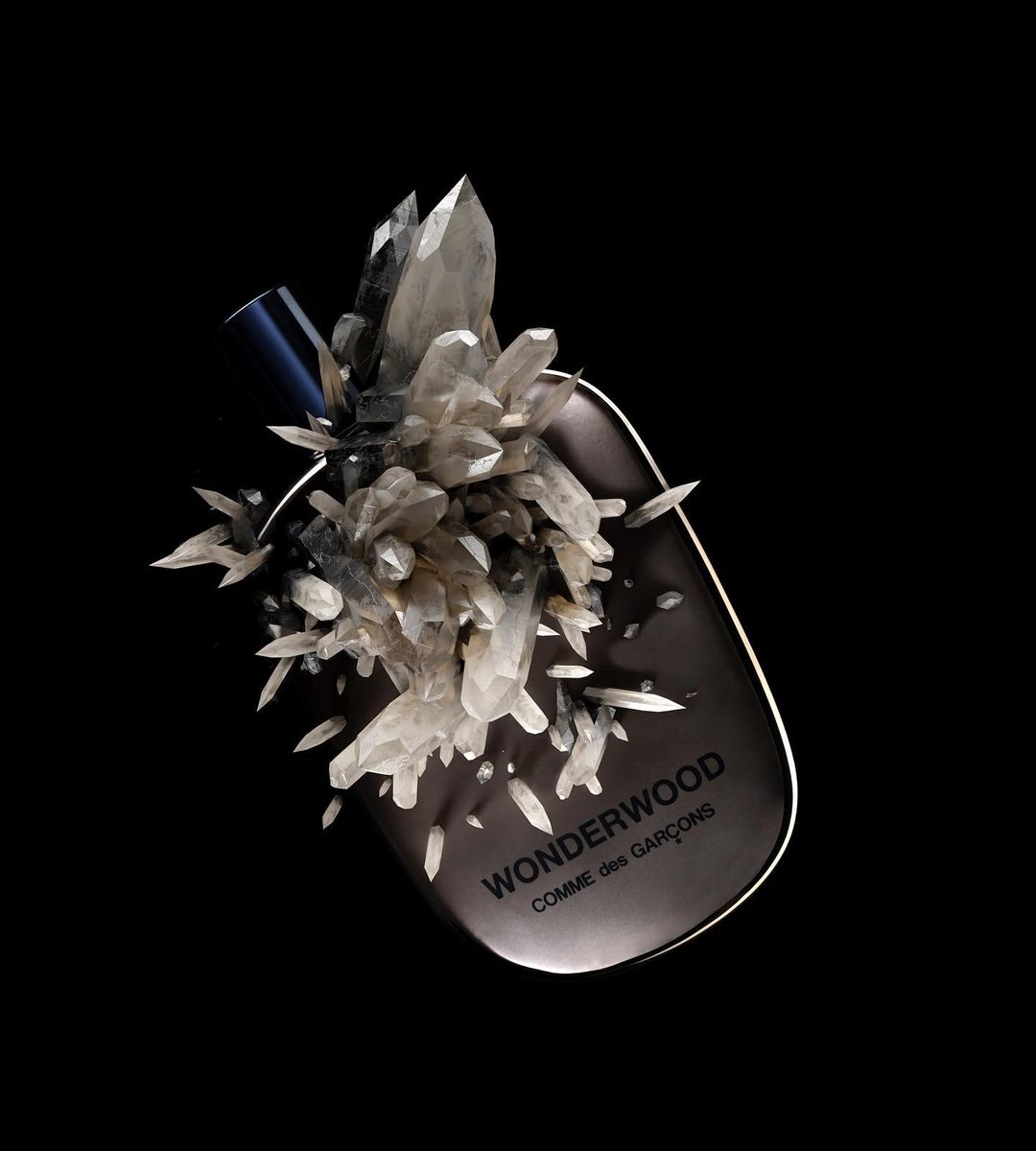 Wonderwood Comme des Garçons fragrance bottle with quartz crystals against a black background in a studio setting for beauty/fashion.