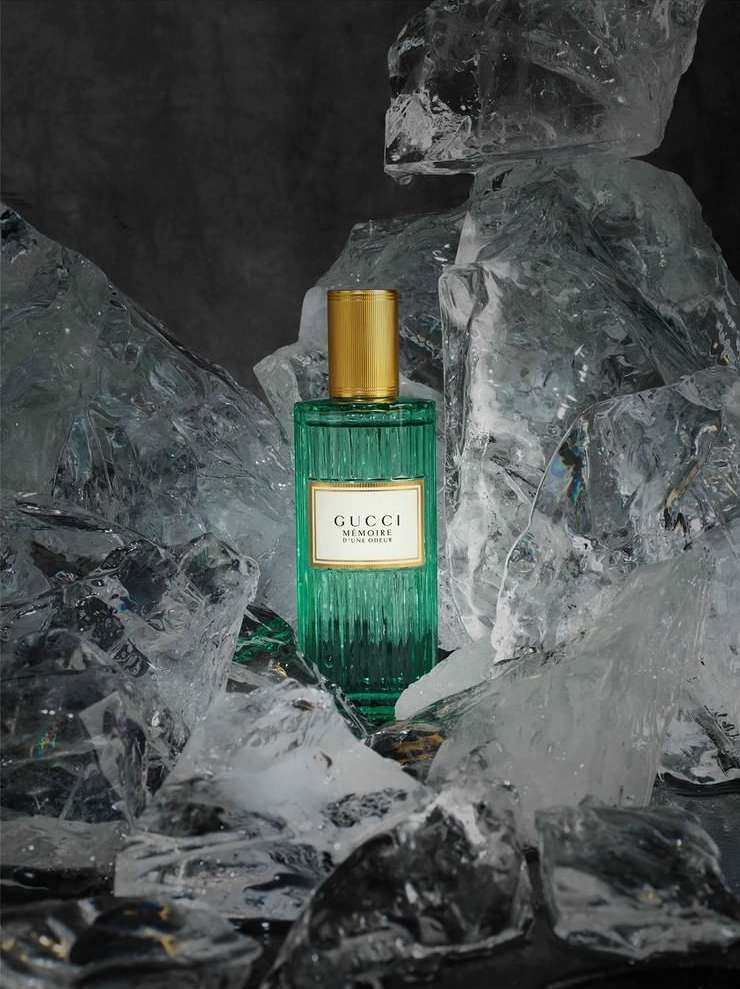 Turquoise perfume bottle with gold cap by Gucci, frozen in ice, against a dark background creating a striking beauty and fashion product shot.