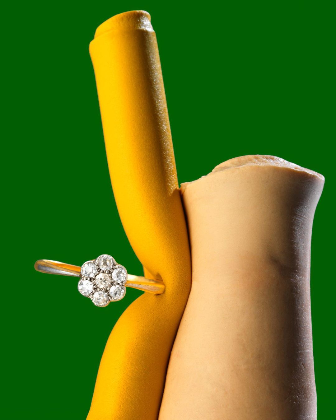 Close-up of a daisy-shaped diamond ring on yellow and tan fabric against a green background, focusing on the jewelry.