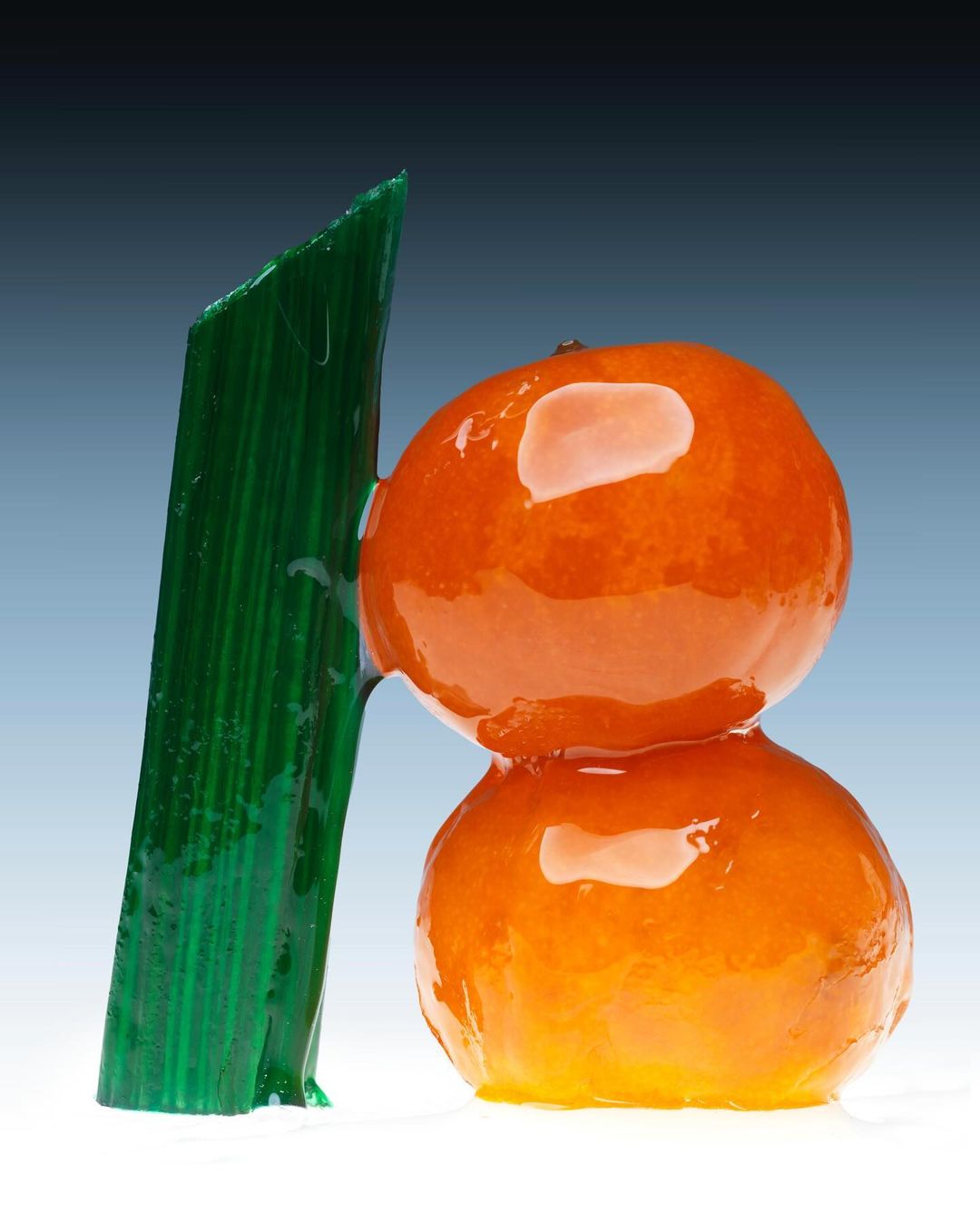 Two mandarin oranges stacked with a green rock candy stick, against a graduated blue-to-white background, studio lighting, and food photography.