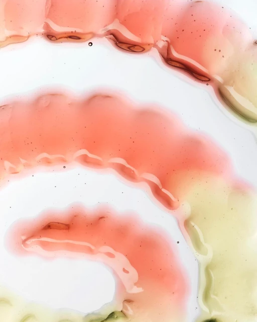 Abstract close-up of transparent liquid with swirling peach, yellow, and brown hues on a white surface, revealing a smooth, organic texture.
