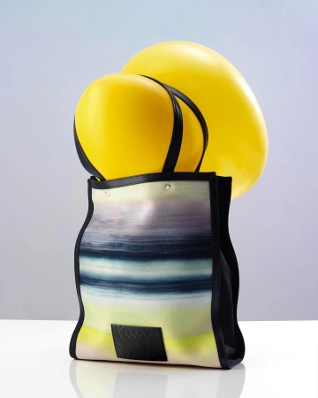 A patterned tote bag with black trim filled with two large yellow balloons against a white background.