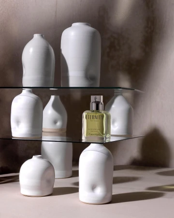 Glass shelves holding white ceramic vases and a glass perfume bottle in a studio setting photographed by Lydia Whitmore