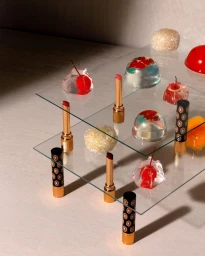 Cosmetic lipsticks and translucent jelly candies arranged on two stacked glass shelves on a textured neutral background