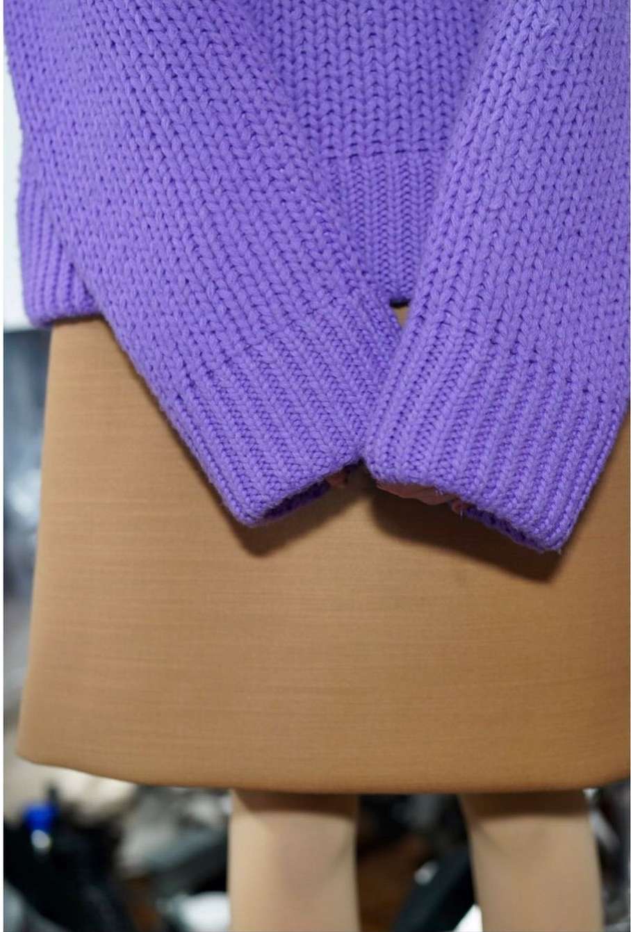 Close-up of a person wearing a purple knit sweater and a brown skirt; the shot focuses on the sweater's texture and color.
