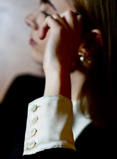 Elegant woman in a black blazer and cream-colored blouse with buttoned sleeves, close-up shot. Focus on the textures and fine details.