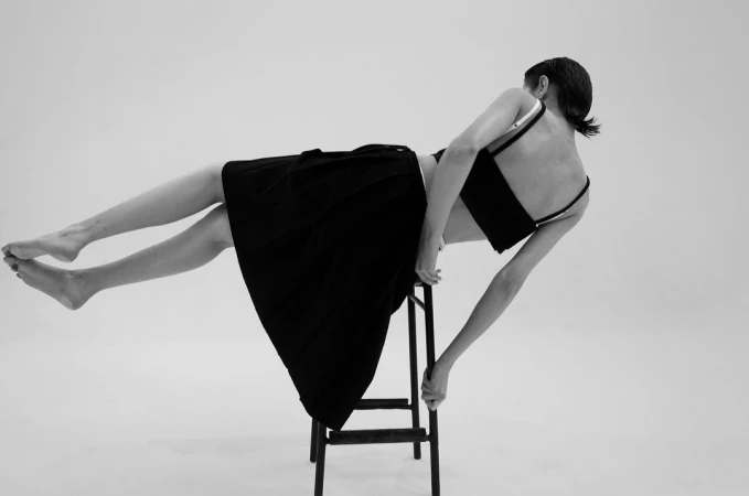 Monochrome fashion editorial featuring a model posing horizontally on a stool against a plain background