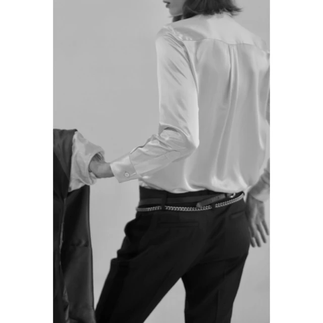 Black and white fashion shot of a woman in a light-colored shirt and dark pants, viewed from the back, with a jacket in hand.