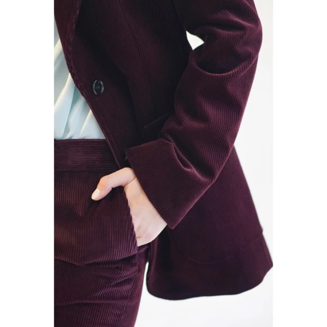 Close-up of a burgundy corduroy blazer and matching pants on an adult, featuring hand in pocket and a light blue shirt underneath.
