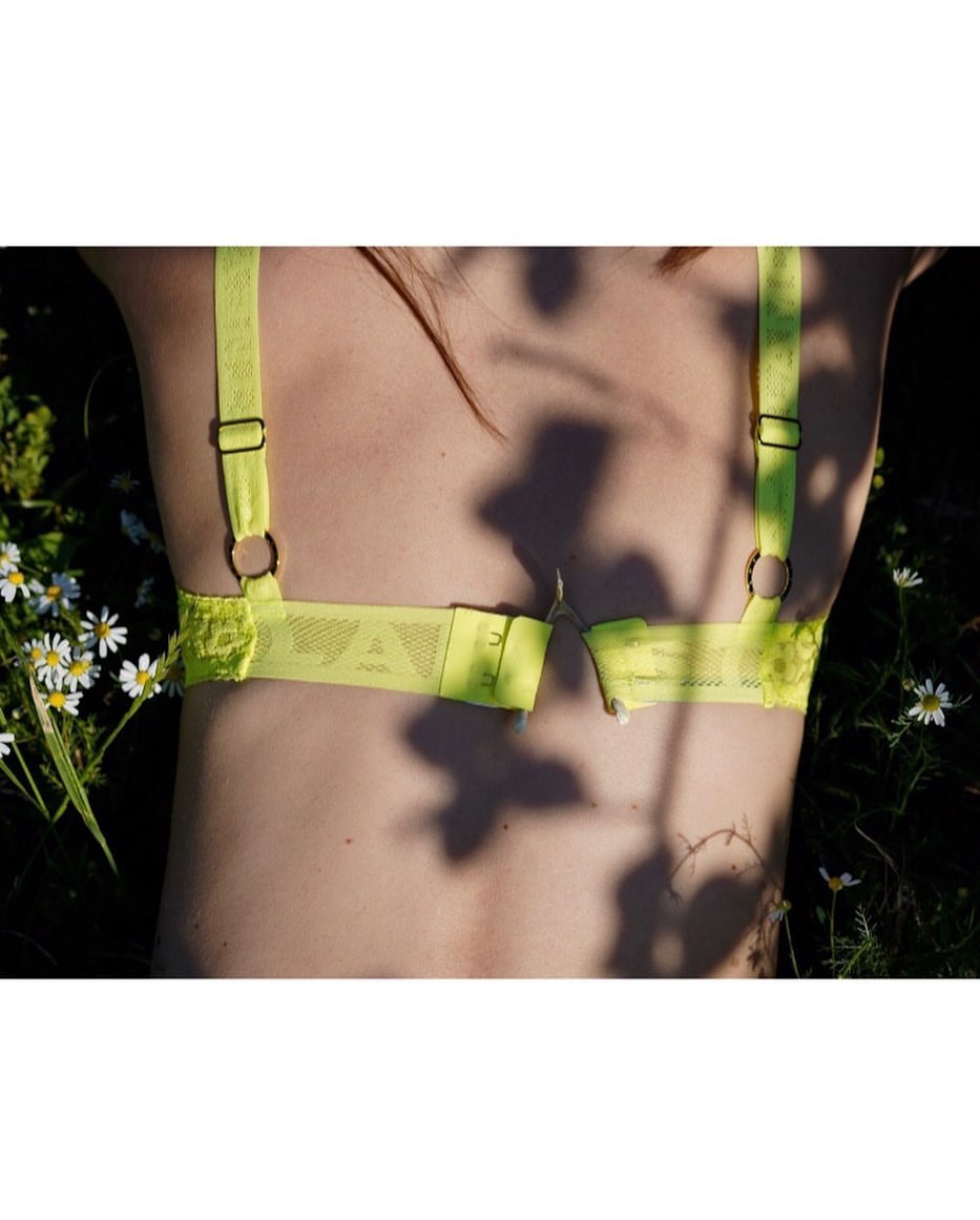 Back view of a woman in a neon yellow bra lying in a field of daisies in natural light, capturing the essence of summer fashion.