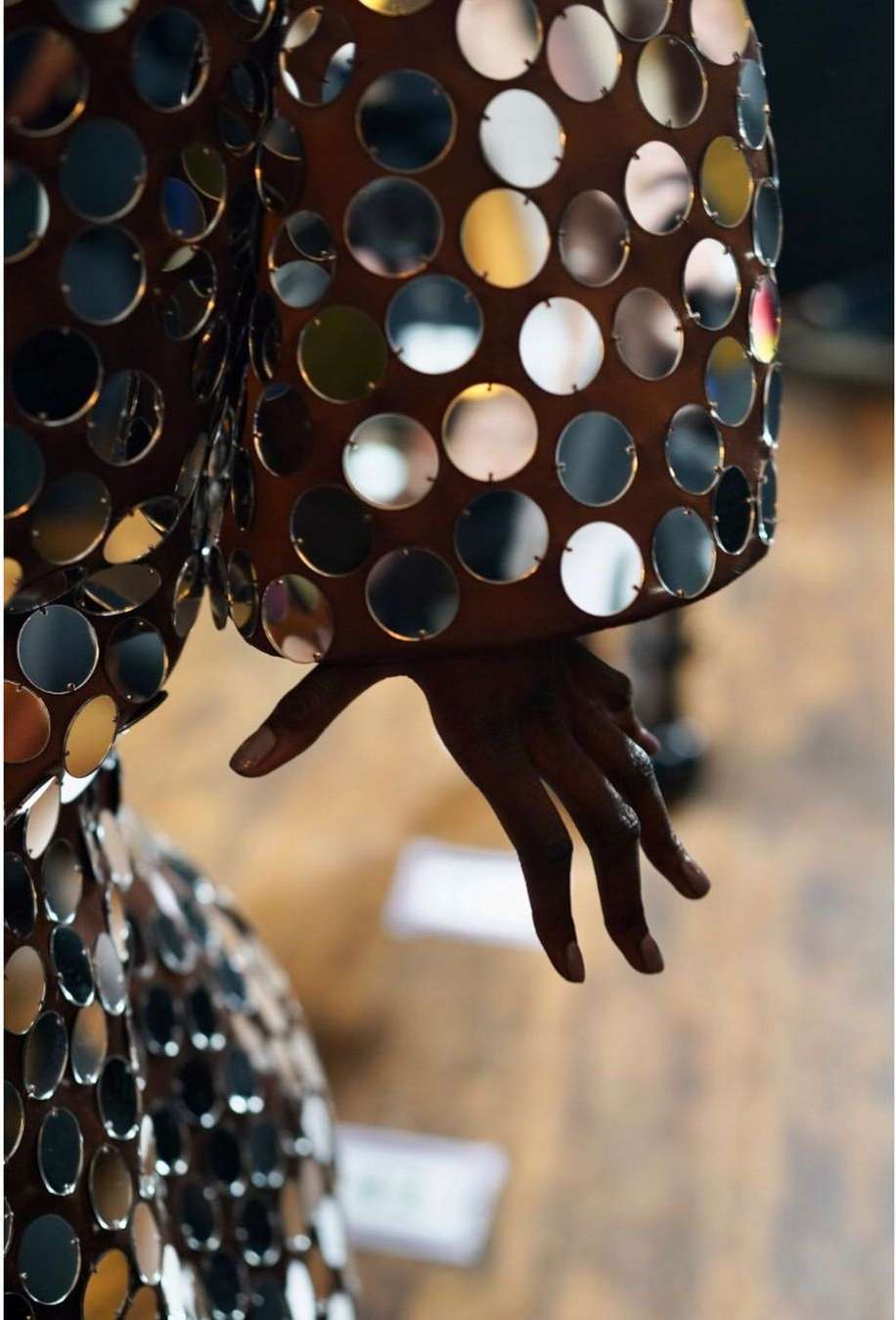 Close-up of fashion model wearing a reflective, polka-dot dress with brown underlay; their arm is bent, and their hand extends into the frame.