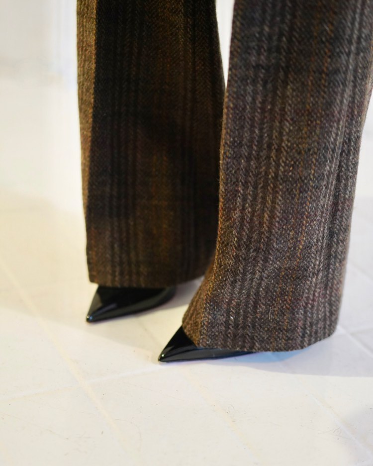 Close-up of tweed flared pants paired with glossy black point-toe shoes on a white surface, showcasing a blend of textures.