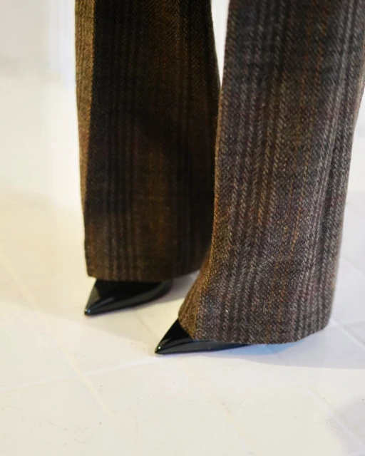 Close-up of tweed flared pants paired with glossy black point-toe shoes on a white surface, showcasing a blend of textures.