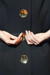 Close-up of hands fastening a large reflective button on a dark tailored coat by photographer Lynette Garland in London.