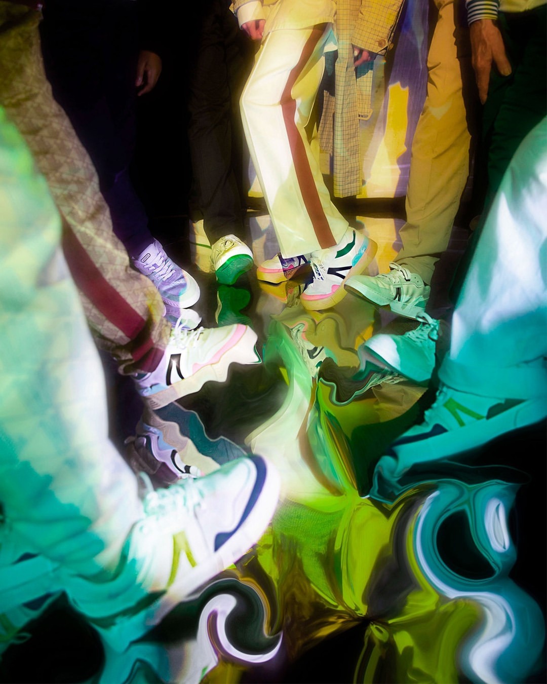 A group of people stand on a reflective floor, wearing various pants and colorful sneakers, creating an abstract and surreal composition.