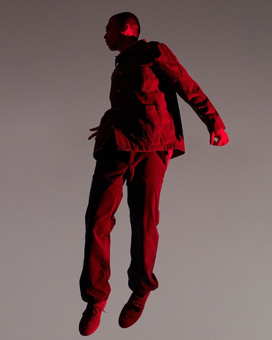 Man suspended in mid-air wearing red jacket and matching trousers against a stark grey studio background