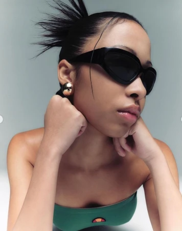 Portrait of a woman wearing black sunglasses and a green strapless top against a light grey background