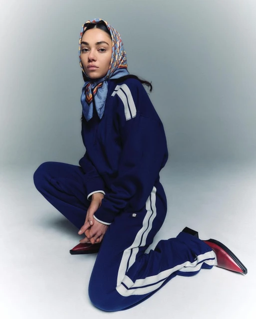 Young woman in blue tracksuit and headscarf squats in a studio. The image highlights fashion and studio portraiture, suitable for search and discovery.