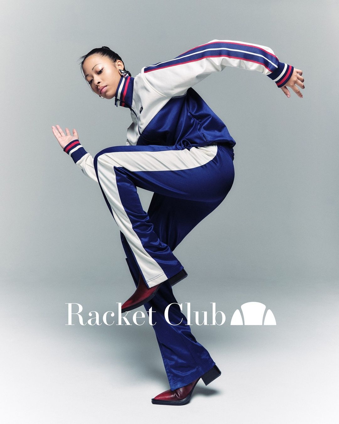 Stylish woman in retro tracksuit strikes dynamic pose against neutral background. High fashion meets vintage sportswear aesthetic.
