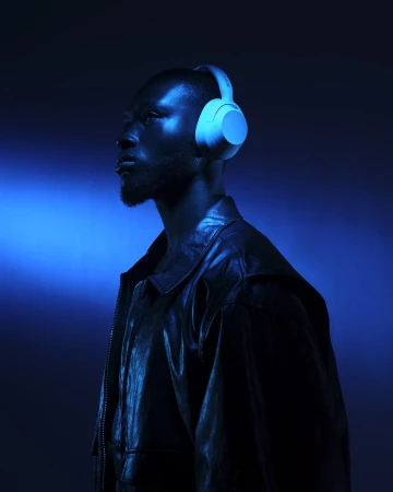Profile of adult male wearing headphones and leather jacket in a dark, moody setting with blue lighting.