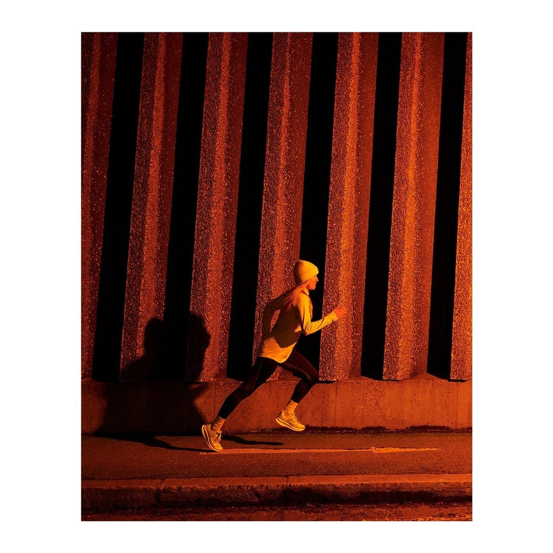 Runner in yellow beanie and jacket running past textured vertical pillars at night