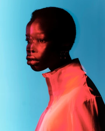 Close-up portrait of a Black woman with short hair wearing a high-neck jacket, lit by dramatic red and blue studio lighting.