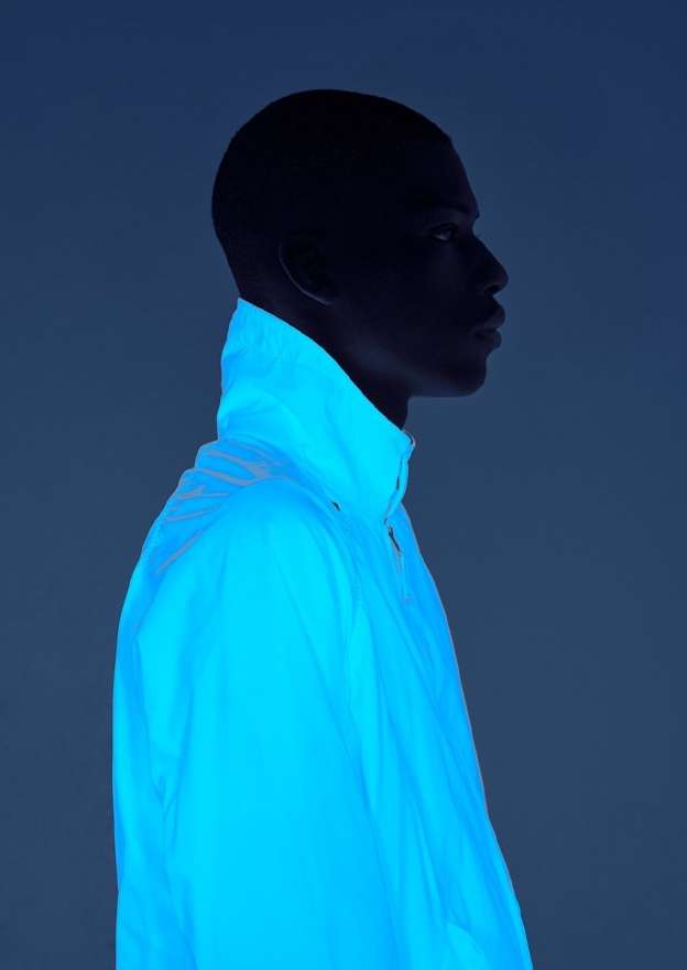 Profile of Black man in blue light wearing a white jacket. Dark silhouette and bright jacket create a striking, modern studio portrait.