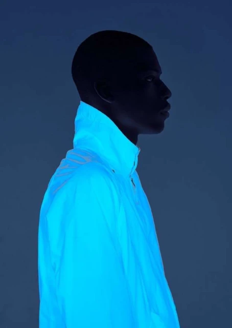 Profile of Black man in blue light wearing a white jacket. Dark silhouette and bright jacket create a striking, modern studio portrait.