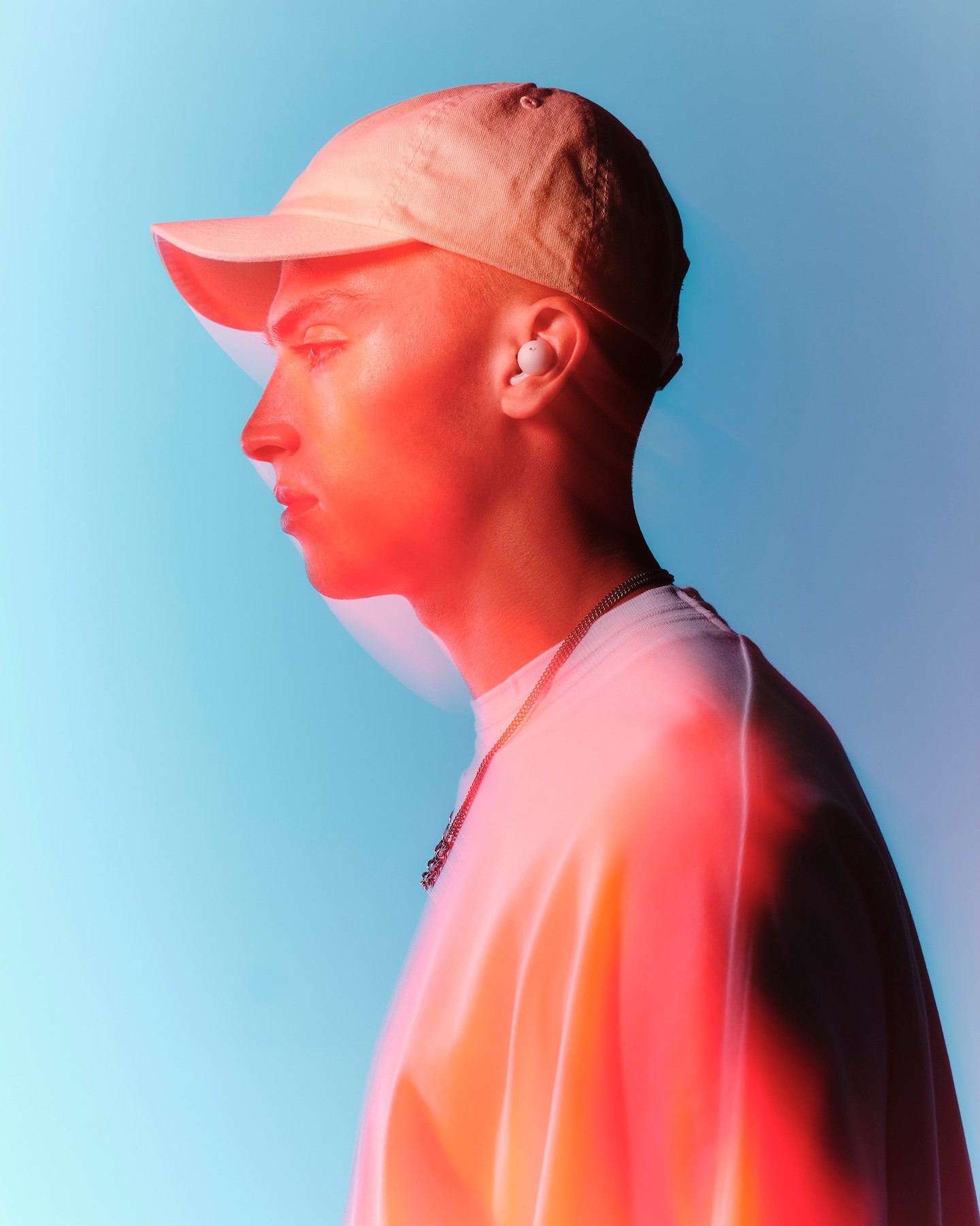 Profile of a young adult man in a cap and white t-shirt, accented by red and blue lighting, showcasing a modern, vibrant aesthetic.