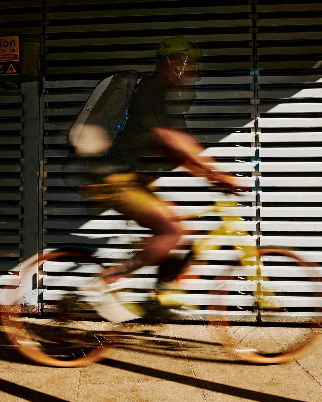 Cyclist in motion blurred across a slatted metal wall, captured by Mads Perch