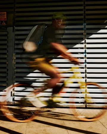 Cyclist in motion blurred across a slatted metal wall, captured by Mads Perch