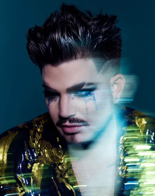 Close-up portrait of a man with styled dark hair, wearing a gold and black jacket with glitter makeup under his eyes.