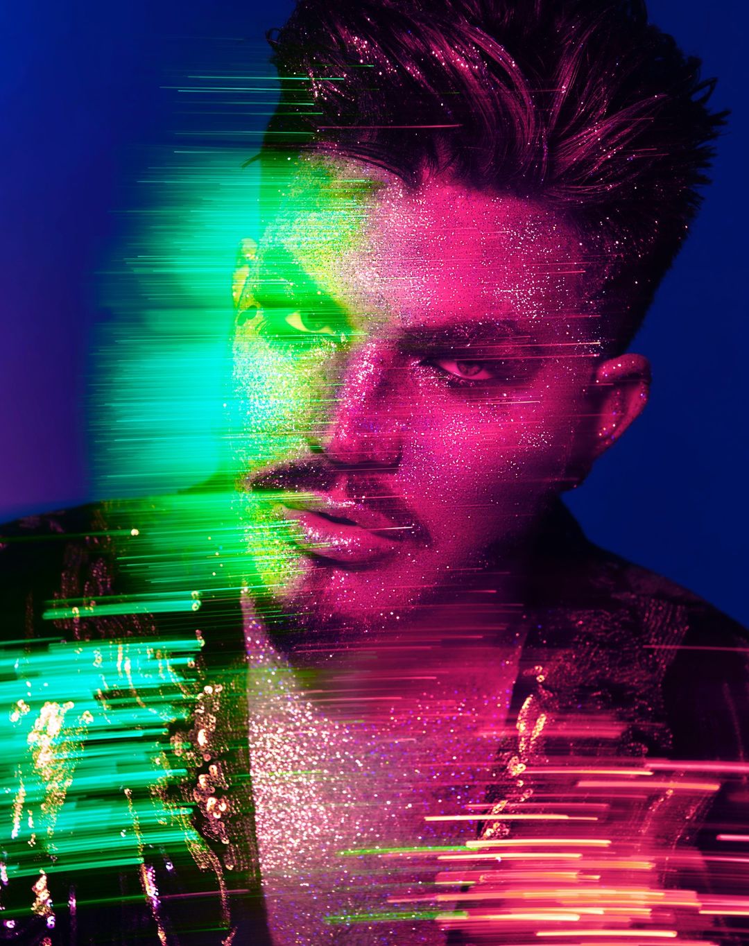 Portrait of a man with dark hair and pink glitter, against a blue background, enhanced with green and red light streams and texture.