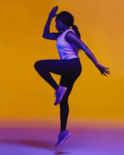 Athletic woman in activewear dynamically posing mid-air against a vibrant orange backdrop, showcasing fitness and energy in studio setting.