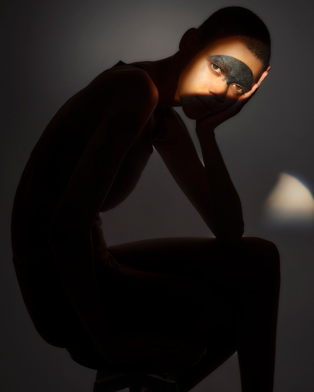 Woman with face mask in dark lighting. Close-up portrait of person sitting with light across the face and shadow silhouette background.