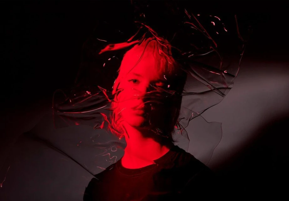 Portrait of person with red lighting and plastic wrap against dark background, showcasing artistic expression and unique visual style.