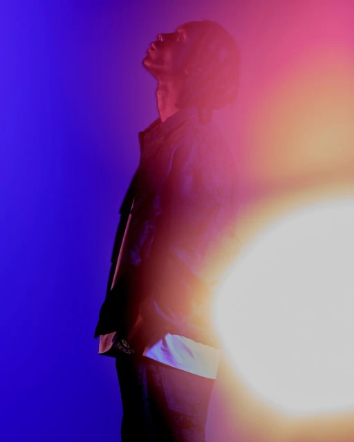 Portrait of an adult male with short hair looking upwards in a studio environment with blue and yellow lighting, and a light leak.